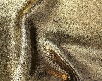 May include: Close-up of a gold metallic fabric with a textured surface. The fabric is wrinkled and folded, creating a dramatic effect.