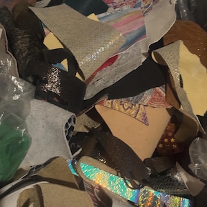 May include: A pile of leather scraps in various colors and textures. Pieces include silver, black, and iridescent materials, along with floral and patterned fabrics. The scraps vary in size and shape, suitable for crafting.