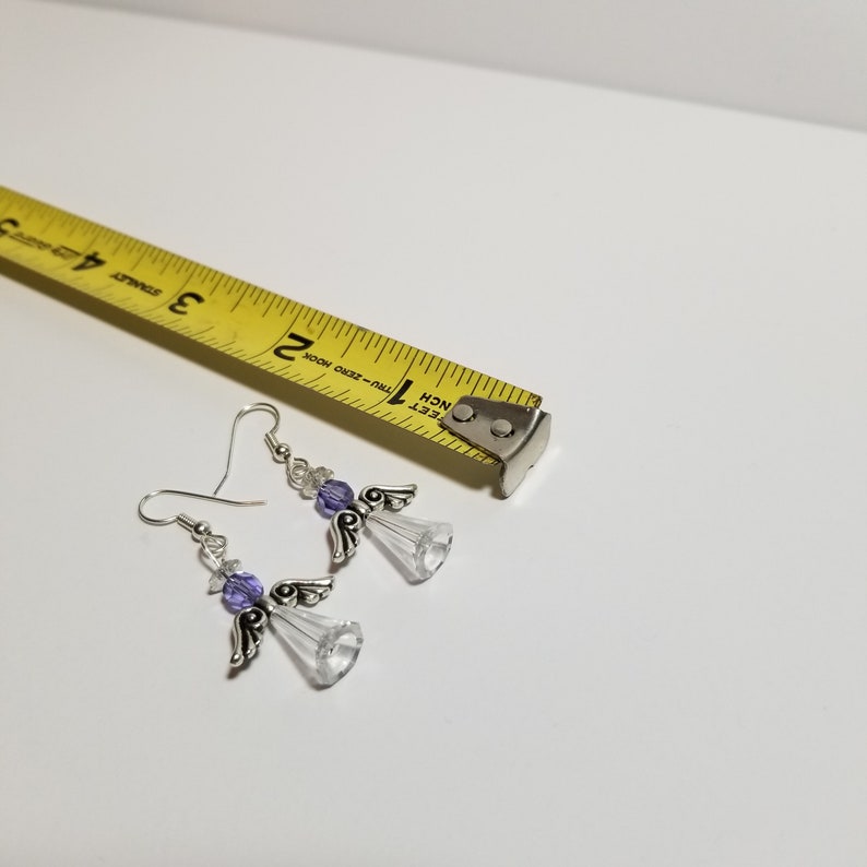 May include: A pair of silver angel dangle earrings with purple crystal beads. The earrings are approximately 2 inches long.