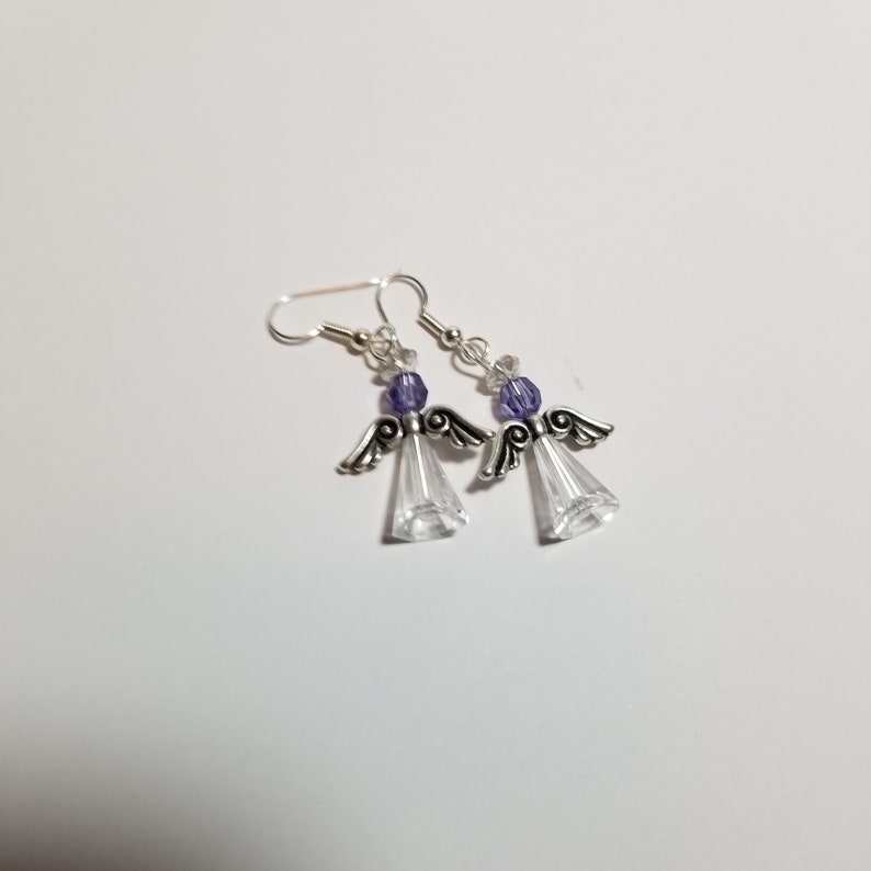 May include: A pair of silver angel-shaped earrings with clear crystal accents and purple beads.