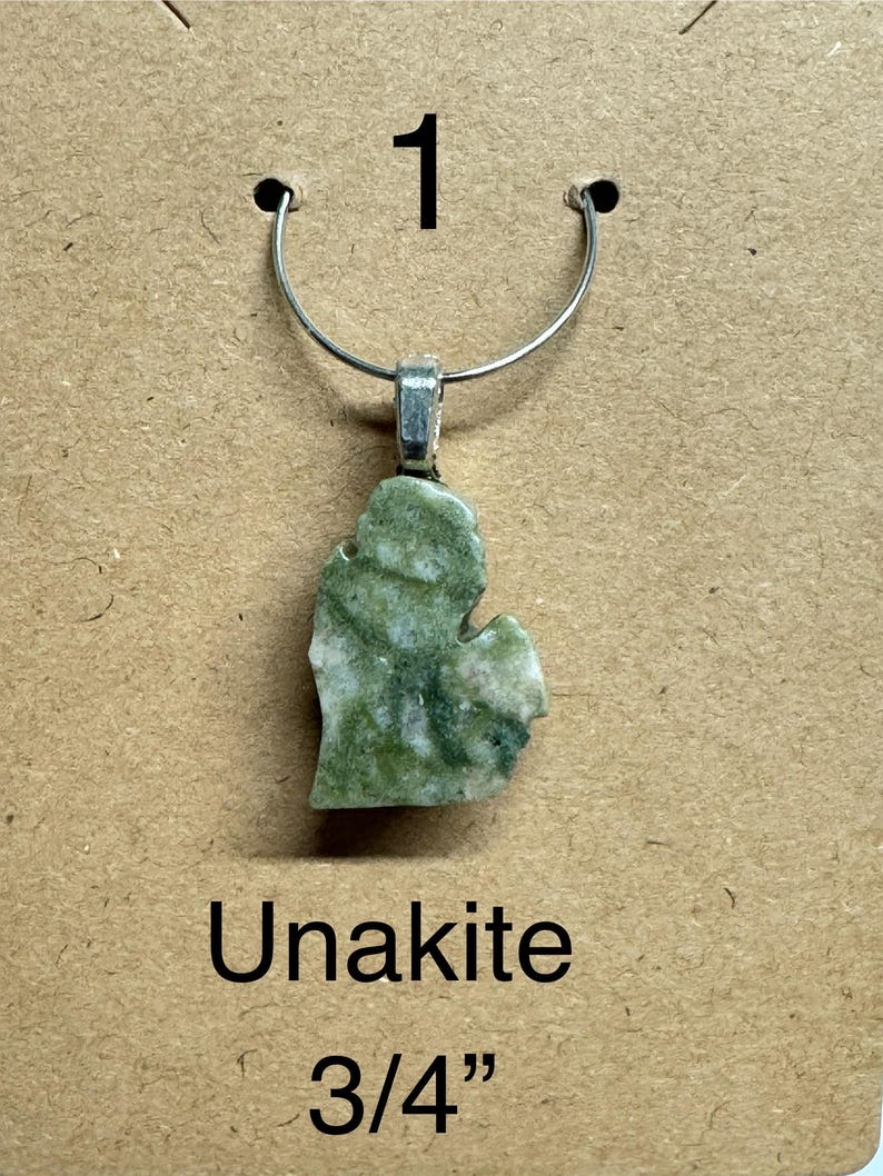 May include: A green and white Unakite pendant in the shape of the state of Michigan, suspended from a silver-colored metal loop. The pendant measures 3/4 inch. The word "Unakite" is printed below the pendant.