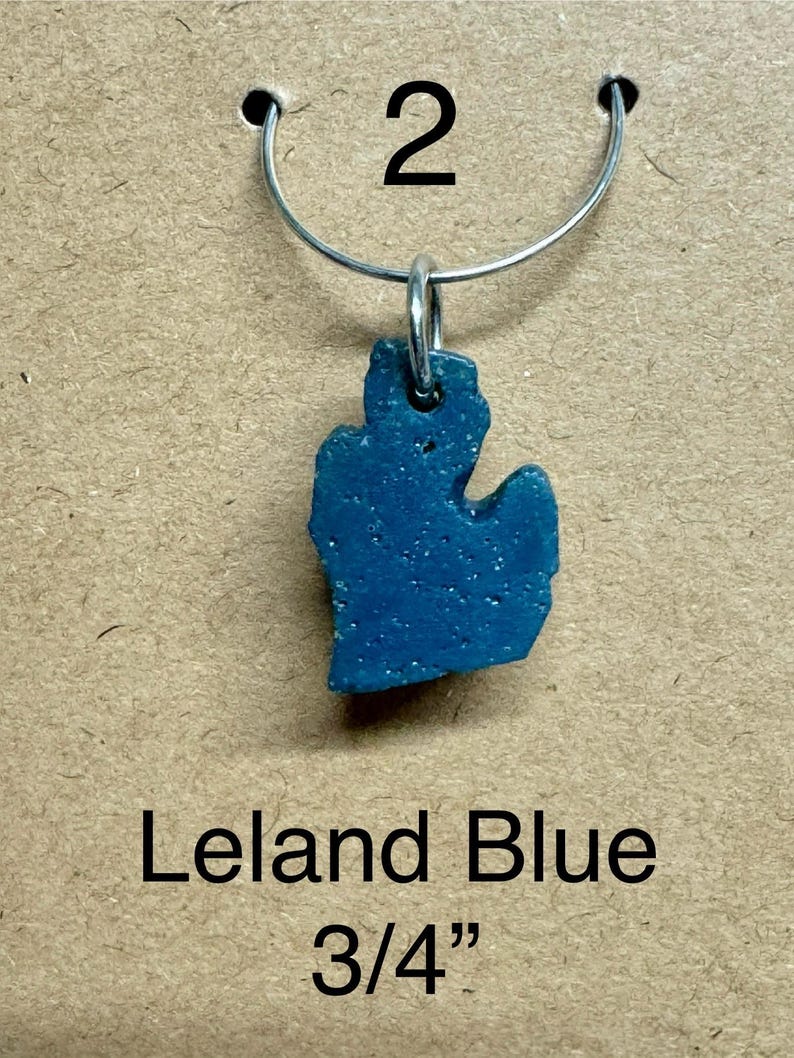 May include: A blue pendant in the shape of the state of Michigan, suspended from a silver-colored metal ring. The pendant is labeled "Leland Blue" and measures 3/4 inch.