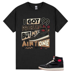 Puede incluir: Camiseta negra con un gráfico de una zapatilla alta negra y roja y el texto "I Got 99 Problems But My Ain't One." También se muestra una zapatilla a juego en la parte inferior de la imagen.
