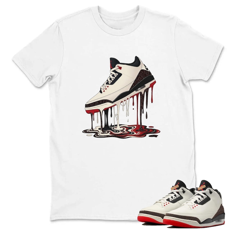 May include: White t-shirt with a graphic of a white and black trainer with red detailing, depicted with dripping black and red paint. A pair of matching trainers are shown at the bottom. The shirt is a casual wear item.
