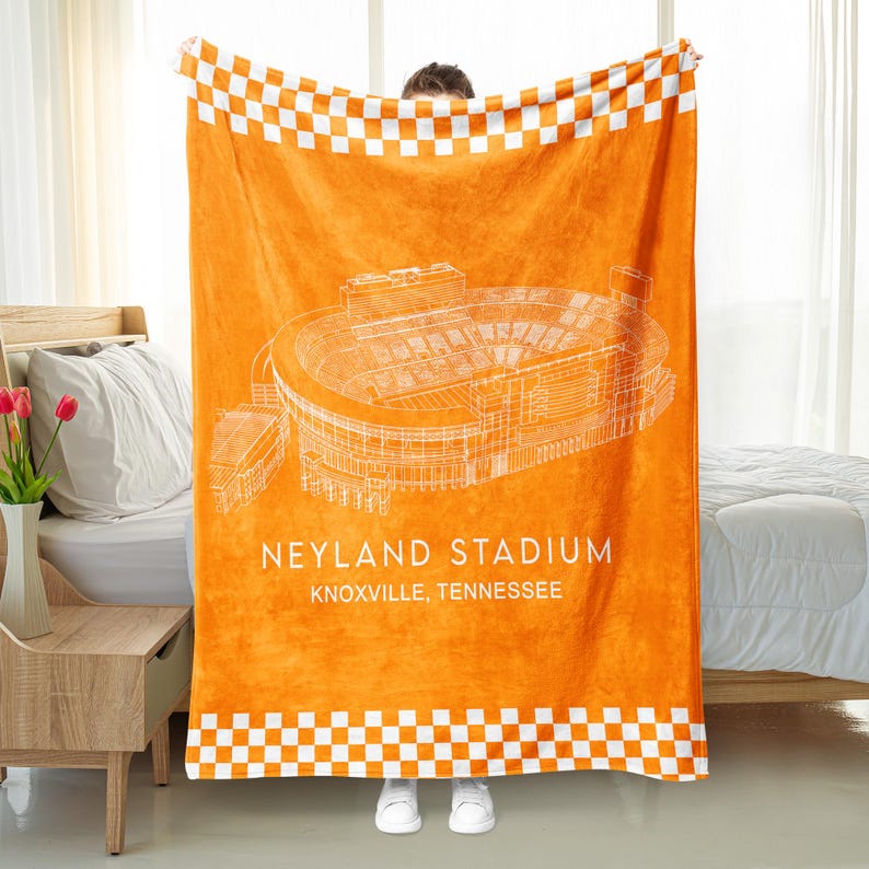 May include: Orange stadium blanket featuring a white architectural drawing of Neyland Stadium in Knoxville, Tennessee. The blanket has a white and orange checkered border.