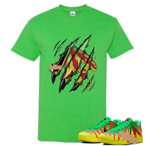 Puede incluir: Una camiseta verde brillante con un diseño de marca de garra que revela un patrón amarillo, rojo y verde. La imagen también muestra un par de zapatillas deportivas verdes y amarillas a juego con detalles en rojo.