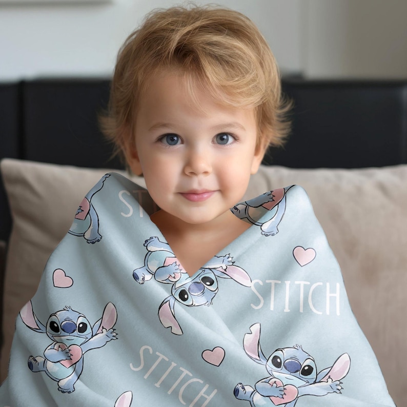 May include: A light blue blanket featuring the character Stitch from the Disney movie Lilo & Stitch. The blanket has a repeating pattern of Stitch, hearts, and the word "STITCH" in white. The blanket is wrapped around a young child.