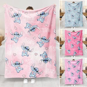 May include: A pink fleece blanket featuring a repeating pattern of the character Stitch holding a heart, with the word "STITCH" and heart shapes scattered across the design. The blanket is displayed in a room setting.