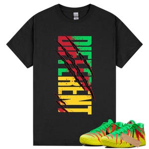 Puede incluir: Camiseta negra con la palabra "DIFFERENT" en verde, rojo y amarillo, con marcas de garras que atraviesan el texto. Un par de zapatillas deportivas verdes y amarillas con detalles rojos se encuentran en la parte inferior de la imagen.