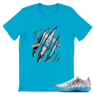 May include: A turquoise t-shirt featuring a graphic design of claw marks tearing through the fabric, revealing a geometric design. A silver and blue athletic shoe is in the lower right corner.