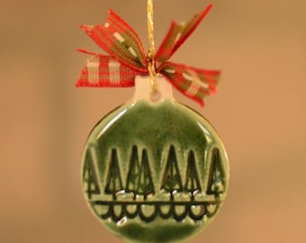 May include: Green ceramic Christmas ornament with a tree design and a red and green plaid ribbon. The ornament is round and has a glossy finish. A gold string is attached for hanging.