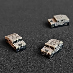 May include: Three miniature toy Humvees in a beige color with black detailing. The vehicles have a black and white logo on the hood.