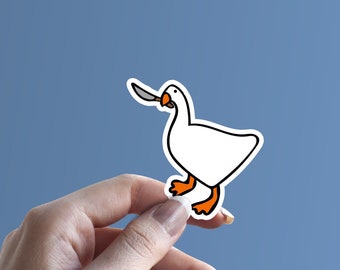 May include: A white goose sticker with a knife in its beak. The sticker is held in a hand against a blue background.