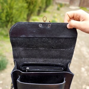 May include: Black leather satchel bag with a flap closure and a brass buckle. The bag has a zippered pocket on the inside and a small pocket on the front.