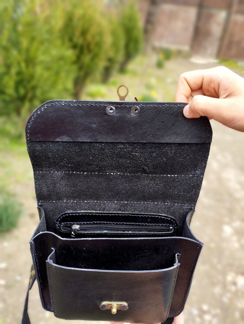 May include: Black leather satchel bag with a flap closure and a brass buckle. The bag has a zippered pocket on the inside and a small pocket on the front.