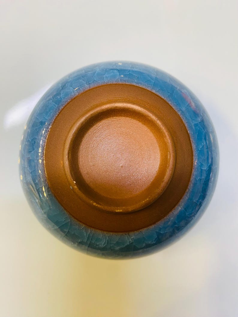 Puede incluir: Un cuenco de cer&aacute;mica con exterior azul e interior marr&oacute;n. La superficie azul tiene un efecto craquelado. El interior del cuenco es de color marr&oacute;n c&aacute;lido. El cuenco probablemente se utiliza para servir alimentos o como objeto decorativo.