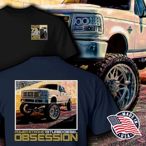 May include: A navy blue t-shirt with a white Ford F-250 pickup truck graphic. The truck is lifted and has large chrome wheels. The text "POWER STROKE 7.3 TURBO DIESEL OBSESSION" is printed in gold on the shirt.