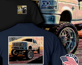 May include: A navy blue t-shirt with a white Ford F-250 pickup truck graphic. The truck is lifted and has large chrome wheels. The text "POWER STROKE 7.3 TURBO DIESEL OBSESSION" is printed in gold on the shirt.