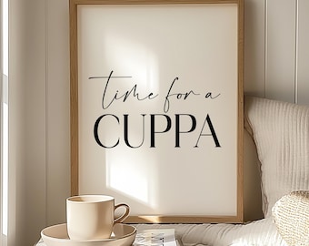 Op de afbeelding: Een ingelijste print met de tekst "Time for a CUPPA" in zwart schrift. Een beige kop en schotel staan op een stapel boeken. De scène wordt verlicht door zacht licht, wat een gezellige sfeer creëert. De print zit in een houten lijst.