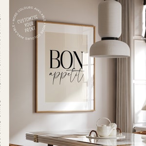 Peut inclure: Une impression encadrée avec le texte "BON appétit" en écriture cursive noire sur un fond beige. L'impression est accrochée à un mur dans une salle à manger avec une table en bois, des chaises et un luminaire suspendu blanc.