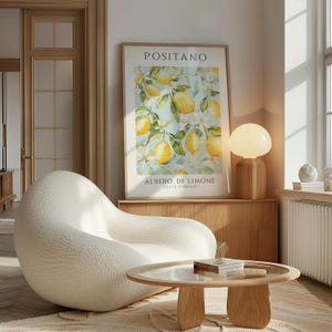 May include: A white, textured armchair sits in a living room with a wooden coffee table and a lamp. A framed print with a watercolor painting of lemons and the text "Positano, Albero di Limone, Costa d'Amalfi" hangs on the wall.