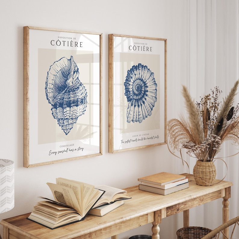 Pode incluir: Duas impress&otilde;es emolduradas com ilustra&ccedil;&otilde;es azuis de conchas. A impress&atilde;o da esquerda apresenta uma concha grande com o texto "Exposition de Cotiere, Coquillage, Every seashell has a story". A impress&atilde;o da direita apresenta uma concha em espiral com o texto "Exposition de Cotiere, Coeur de l'ocean, The softest hearts build the hardest shells".
