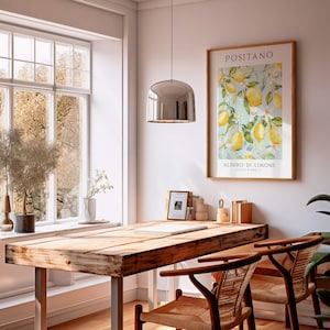 May include: A wooden table with a rustic finish, two wicker chairs, and a silver pendant light hanging above. A framed print with a watercolor illustration of a lemon tree with the text "Positano, Albero di Limone, Costa d'Amalfi" is hanging on the wall.