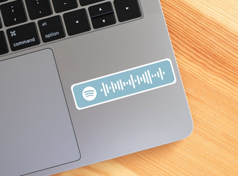 Peut inclure: Un autocollant rectangulaire sur fond bleu clair avec le logo Spotify blanc sur la gauche et un motif de code d'onde sonore blanc s'&eacute;tendant vers la droite. L'autocollant est appos&eacute; sur la surface m&eacute;tallique d'un ordinateur portable.