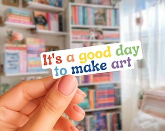 May include: A rectangular sticker with a white background featuring the colorful text It's a good day to make art. The words are written in a playful, rounded font with red, orange, yellow, green, and dark blue letters against the white surface.