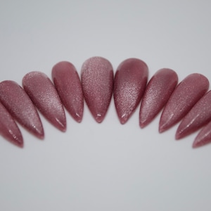 May include: A set of ten long, pointed, pink false nails with a shimmery finish.