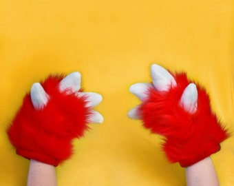 May include: A pair of red fuzzy mittens with white claws. The mittens are on a yellow background.