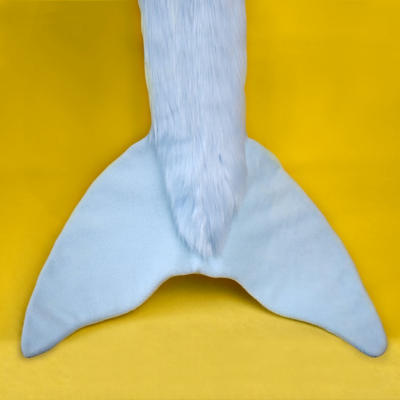 May include: A light blue plush tail with a furry top section and a wide, fan-shaped bottom. The tail is set against a bright yellow background, creating a playful contrast. The tail appears to be part of a costume or toy.