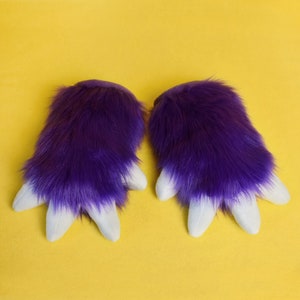 May include: A pair of purple furry hand paws with white claws. The paws are soft and fluffy, and they would be perfect for a costume or cosplay.