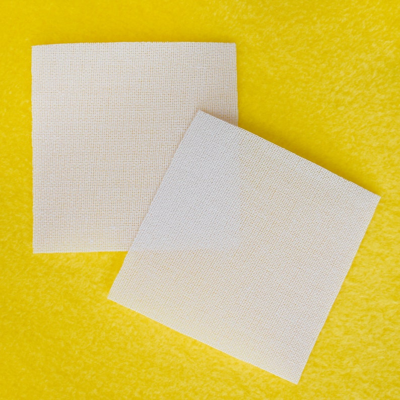 May include: Two white, square, woven fabric placemats on a yellow surface.