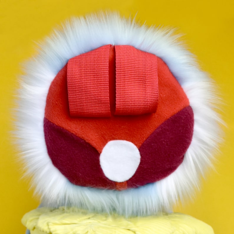 May include: A colorful, whimsical hat with a red top and a white fur trim. The hat features a red ribbon detail and a white circular accent. The hat is set against a yellow background.