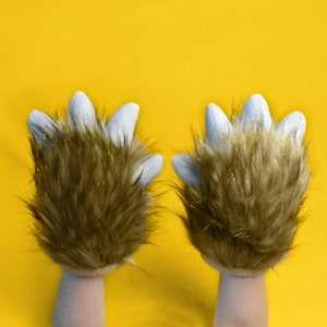 May include: A pair of brown furry gloves with white tips on the fingers, raised in the air against a yellow background.