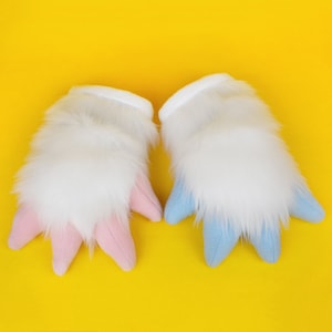 May include: A pair of white furry hand puppets with pink and blue claws. The puppets are on a yellow background.