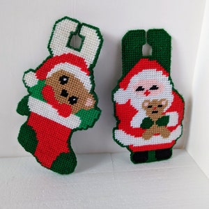 May include: Two Christmas stocking ornaments, one with a Santa Claus holding a teddy bear and the other with a teddy bear wearing a Santa hat. Both ornaments are made of green, red, and white felt.