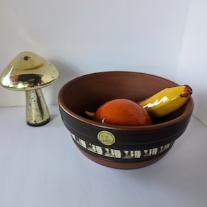 May include: A brown ceramic bowl with a black and white geometric design, filled with a yellow banana and an orange ceramic fruit.
