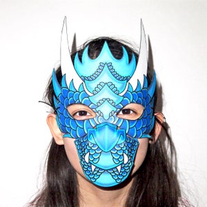 Könnte beinhalten: Eine blaue und weiße Drachenmaske mit weißen Hörnern und einem blauen und weißen Schuppenmuster.