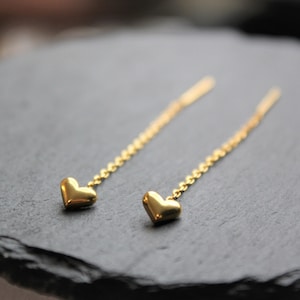 May include: A pair of gold dangle earrings with small heart charms at the end of each chain.