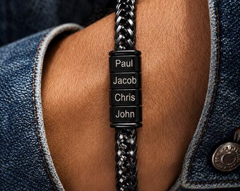 May include: A black braided bracelet with four rectangular beads. Each bead has a name engraved in white: Paul, Jacob, Chris, and John. The bracelet is worn on a wrist, with a denim jacket in the background.