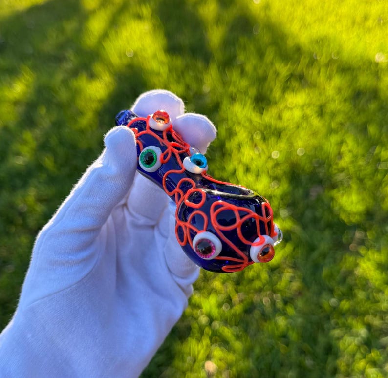 May include: A blue glass pipe with a red and orange swirl design. The pipe is decorated with colorful glass eyes.
