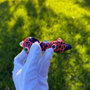 May include: A blue glass pipe with a red and orange swirl design and multiple googly eyes.