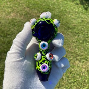 May include: A blue glass pipe with green and white details. The pipe is decorated with multiple colorful eyes.