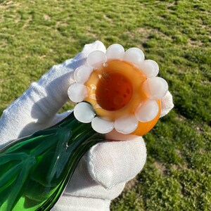 May include: A green glass pipe with a round orange bowl. The bowl is decorated with a ring of white glass beads.