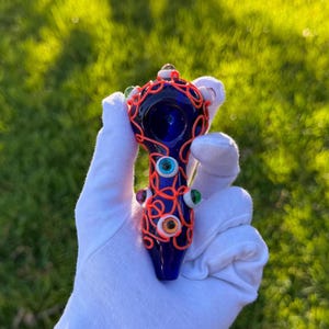 May include: A blue glass pipe with a bright orange wire design and colorful glass eyes.