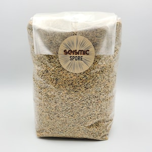 May include: A clear plastic bag filled with light brown rye grain. The bag has a brown paper label with the text "Seismic Spore" in a brown circle with a starburst design.