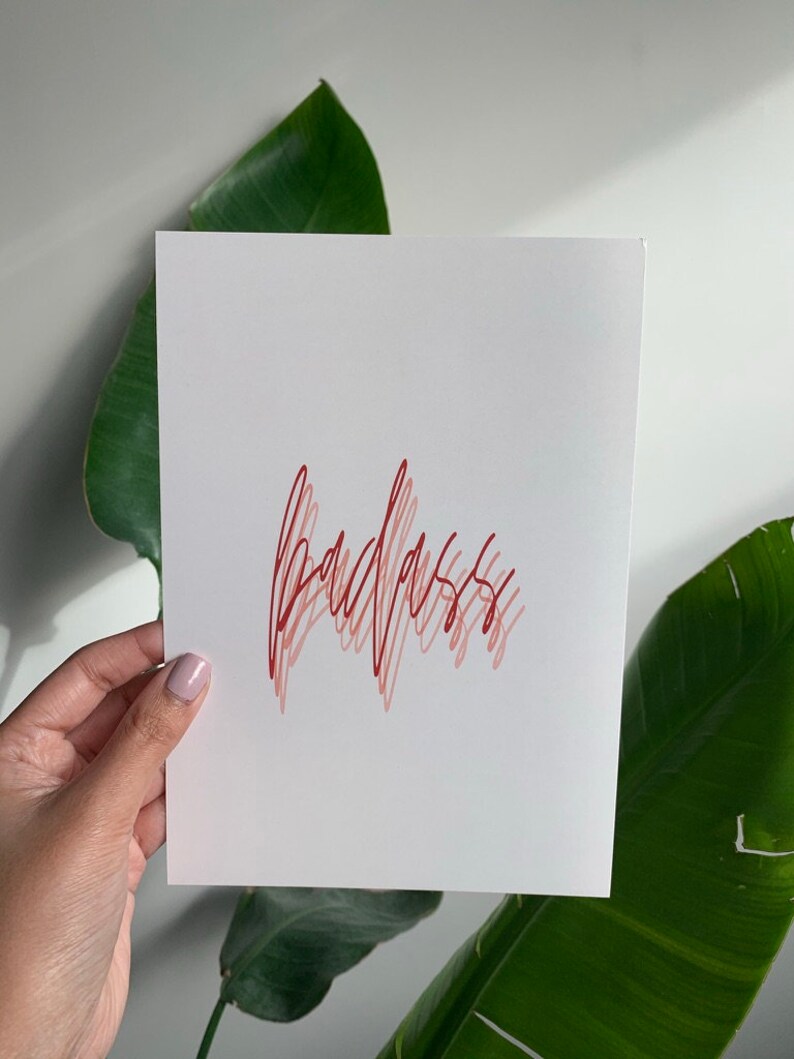 Puede incluir: Una tarjeta blanca con la palabra "badass" escrita en cursiva roja.