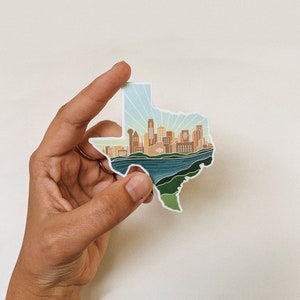 May include: A sticker shaped like the state of Texas with a detailed illustration of the Austin skyline, including the iconic Texas State Capitol building. The sticker features a blue and green color scheme, representing the city's natural beauty.